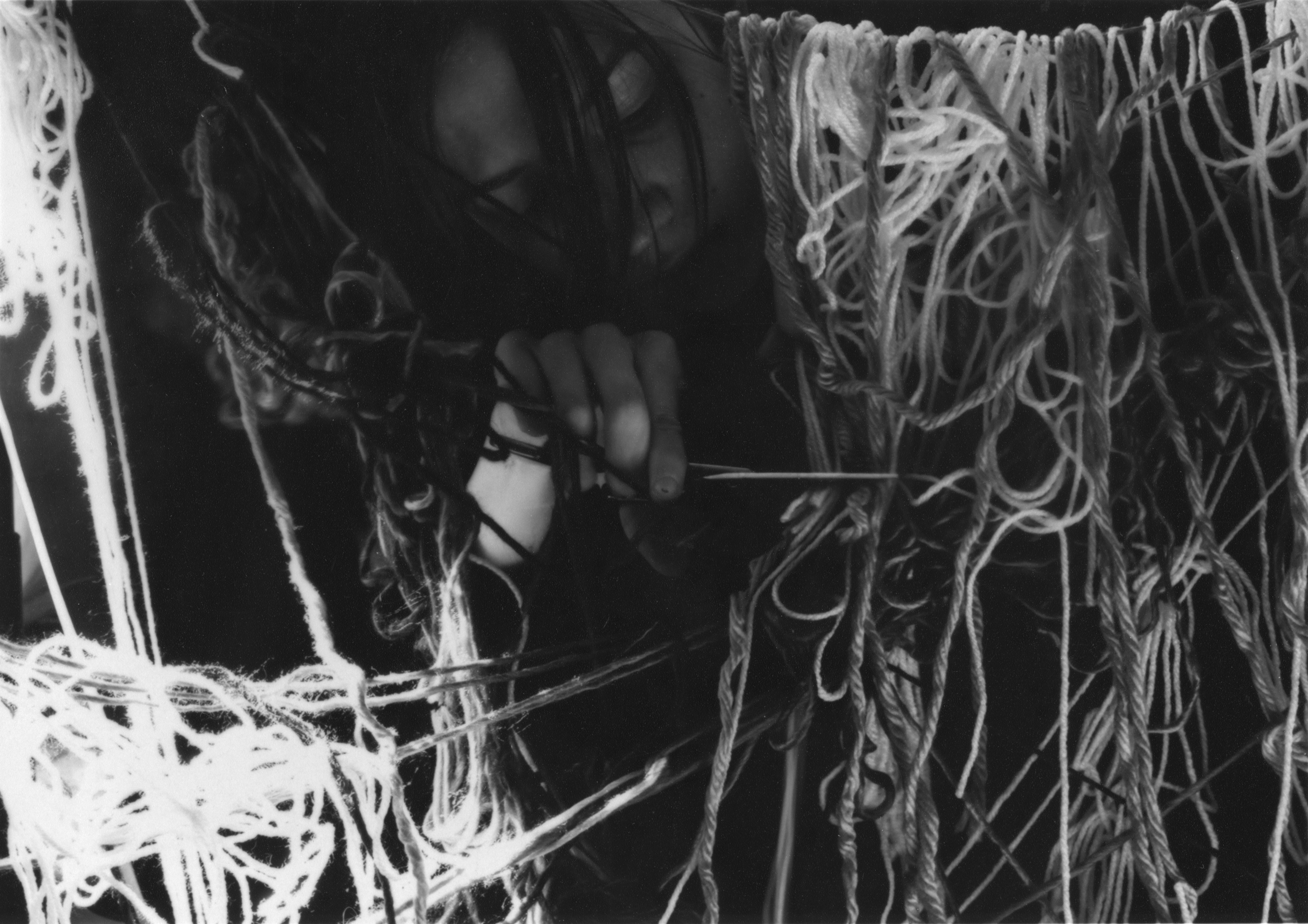 Black and white gelatin silver print of a woman looking down as she cuts through a wall of tangled yarn with scissors